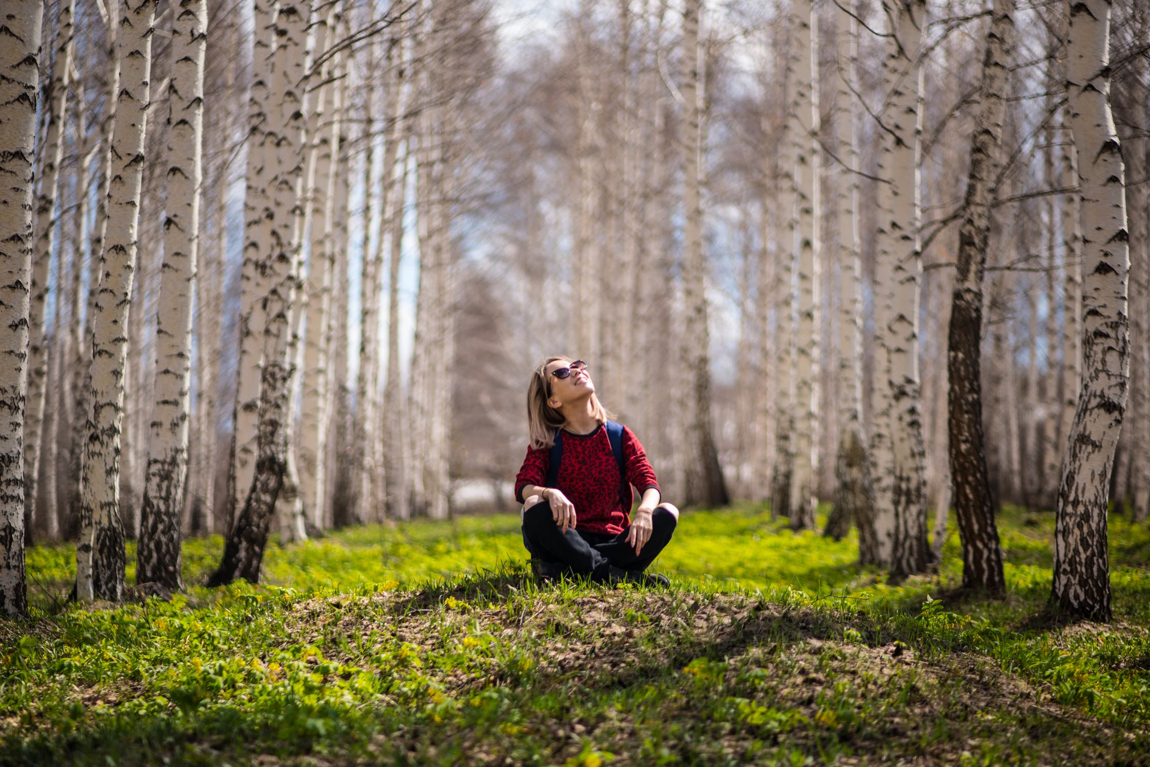Woman sat on the floor smiling and looking up at the trees around her